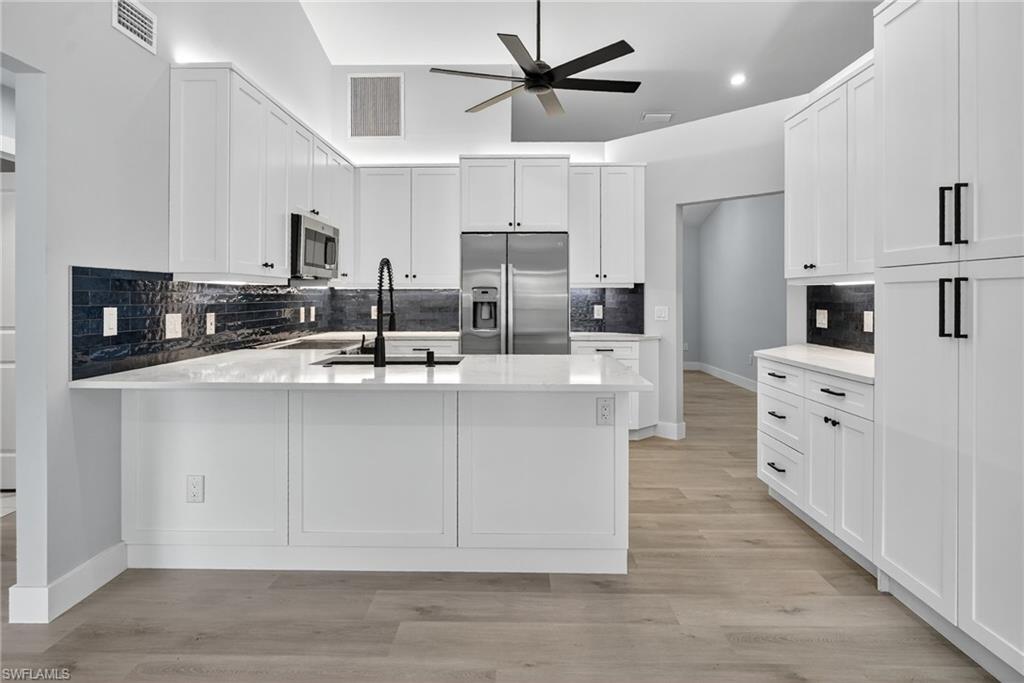 Kitchen featuring a ceiling fan, new GE stainless steel appliances, a peninsula, tasteful backsplash, and white wood cabinets