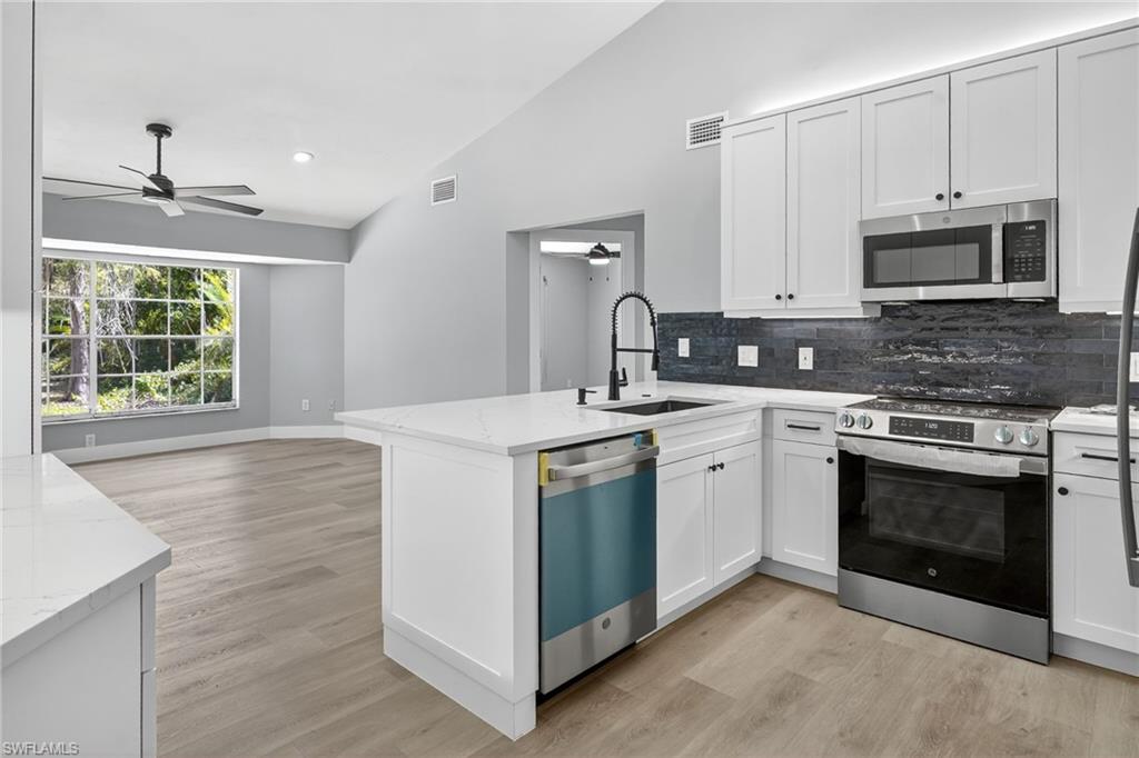 Kitchen featuring vaulted ceiling, stainless steel appliances, a ceiling fan, tasteful backsplash, and light wood-style floors