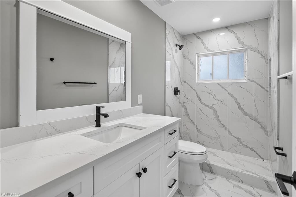 Guest bathroom featuring white wood vanity with Quartz top a marble look shower, and marble look floors,