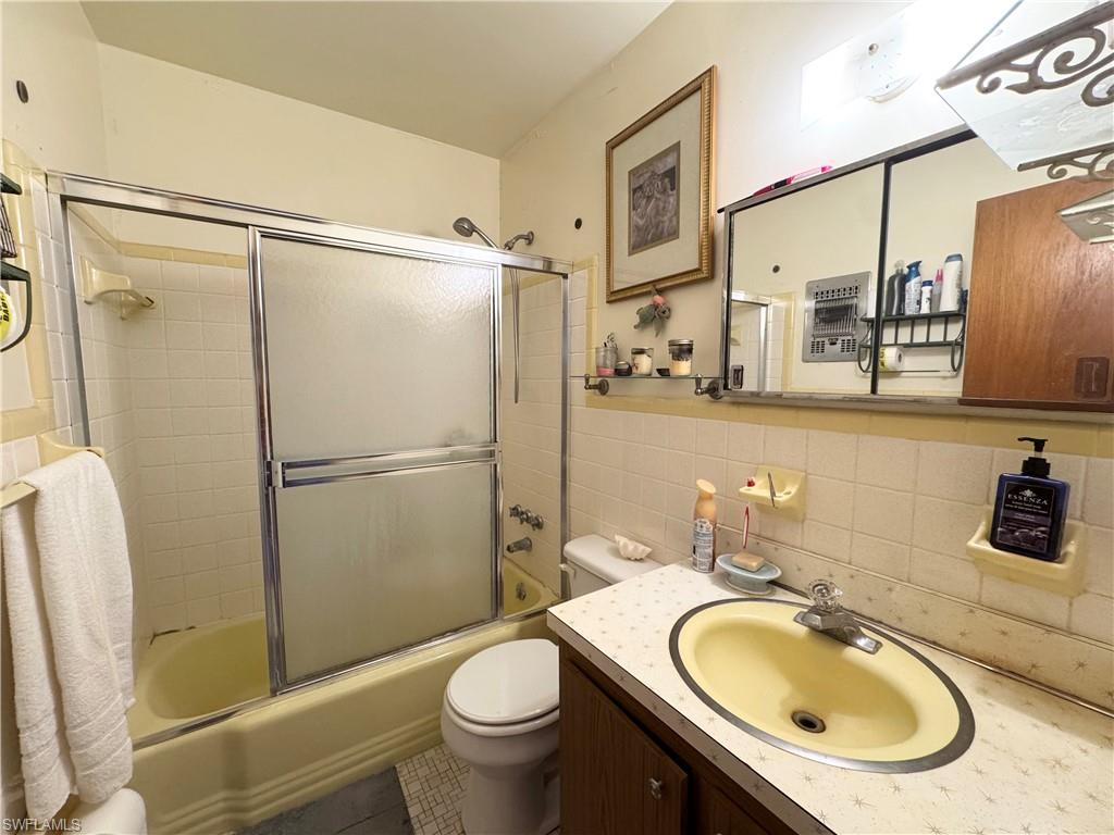 Bathroom with vanity, enclosed tub / shower combo, tile patterned flooring, and tile walls