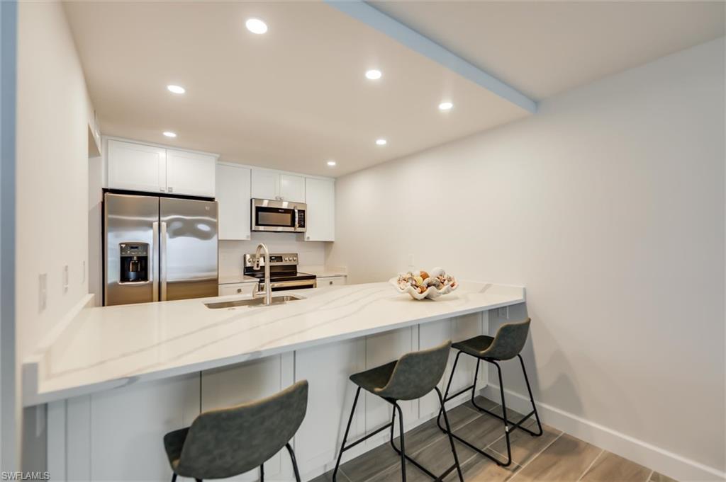 Kitchen with stainless steel appliances, white cabinetry, recessed lighting, and light stone counters