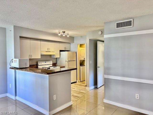Kitchen featuring under cabinet range hood, white appliances, light tile patterned floors, a peninsula, and a textured ceiling