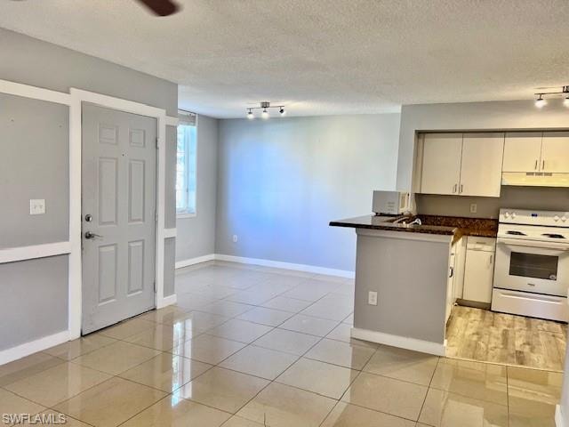 Kitchen featuring white electric range oven, under cabinet range hood, a peninsula, track lighting, and dark countertops