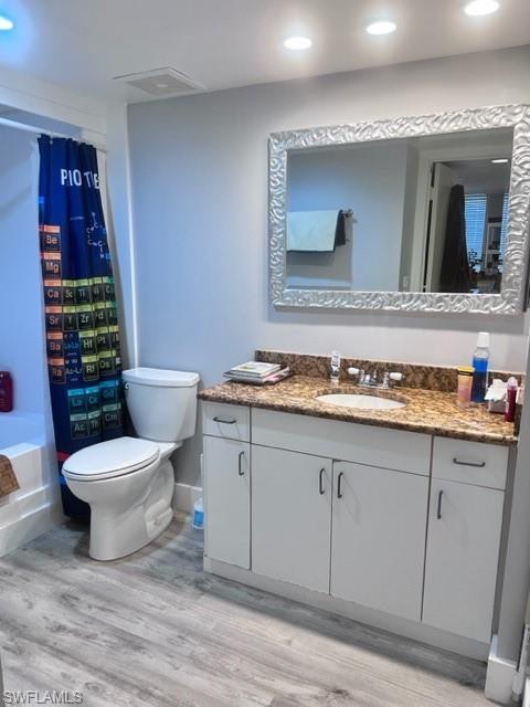 Full bath with vanity, wood finished floors, shower / bathtub combination with curtain, and recessed lighting