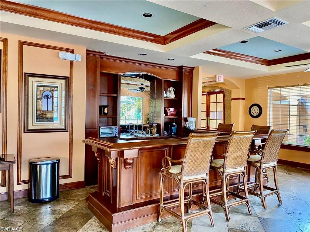 Community bar area featuring stone tile flooring, ornamental molding, arched walkways, ceiling fan, and coffered ceiling