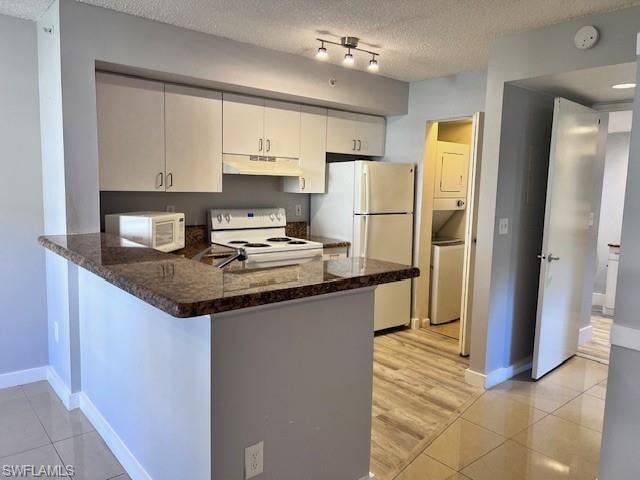 Kitchen with white appliances, under cabinet range hood, a peninsula, light tile patterned flooring, and a textured ceiling