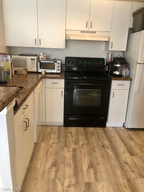 Kitchen with white appliances, under cabinet range hood, white cabinets, and light wood-style floors