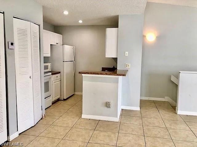 Kitchen with white appliances, light tile patterned floors, white cabinets, a textured ceiling, and dark countertops