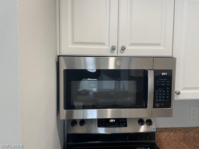 Kitchen view of stainless steel microwave, white cabinetry, and a textured wall