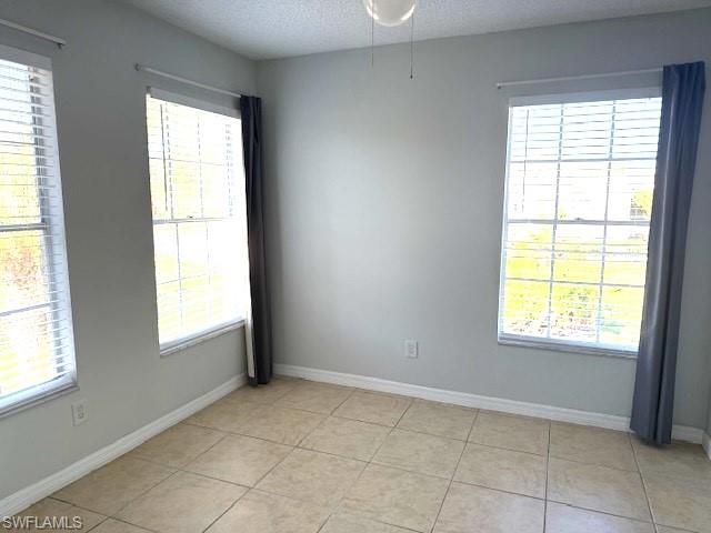 Empty room featuring healthy amount of natural light, light tile patterned flooring, and a textured ceiling