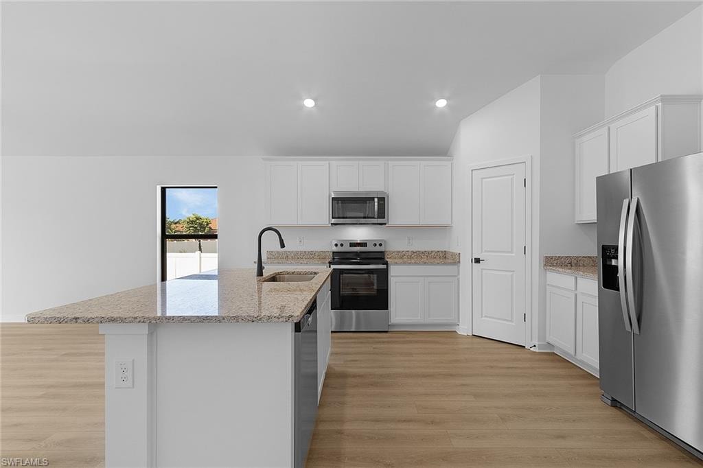 Kitchen with appliances with stainless steel finishes, light wood-type flooring, recessed lighting, a center island with sink, and white cabinets