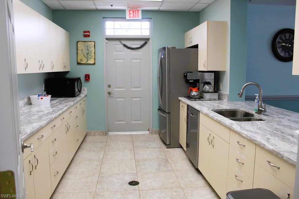 Kitchen with a drop ceiling, black microwave, dishwasher, light stone countertops, and light tile patterned flooring