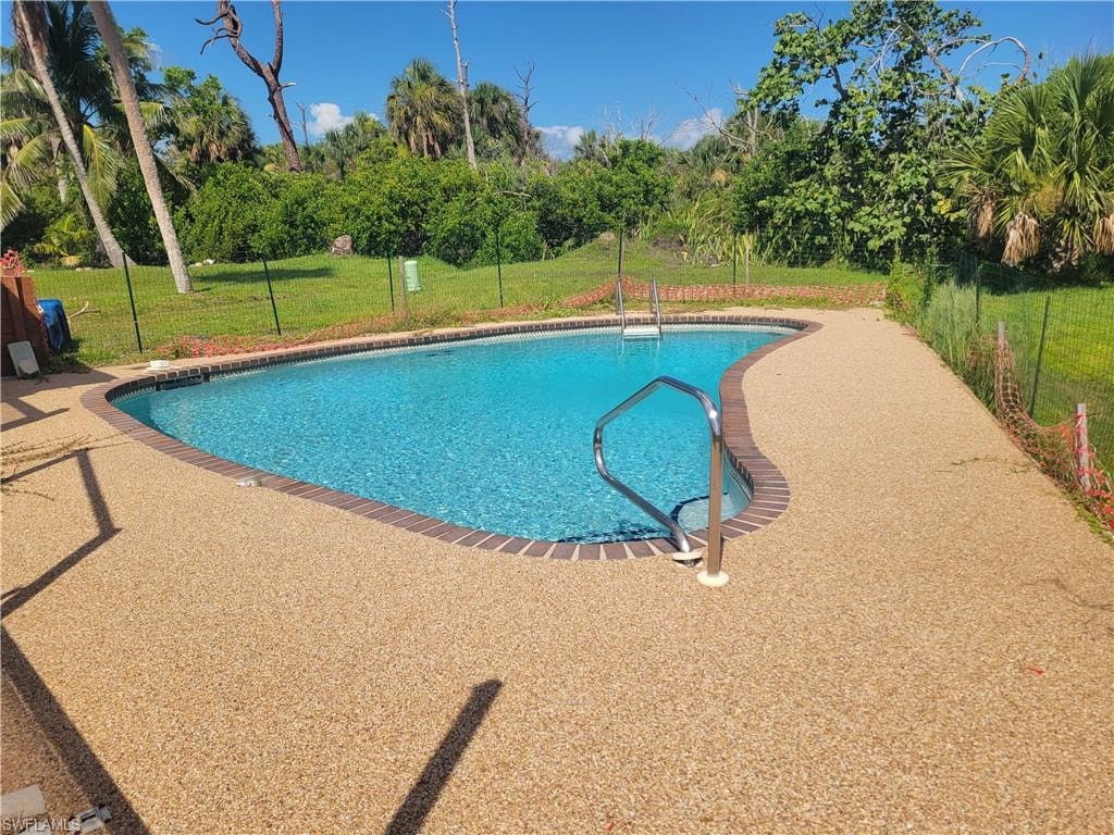 Outdoor pool with a yard, view of scattered trees, and a patio area