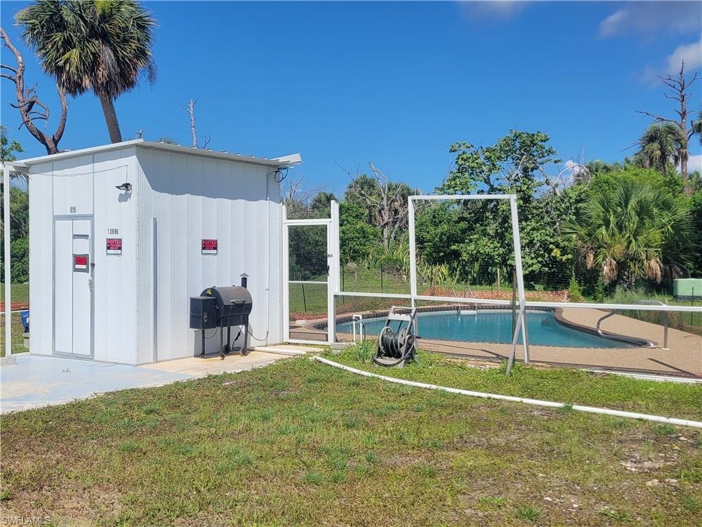 View of swimming pool featuring a grill, a lawn, and an outbuilding