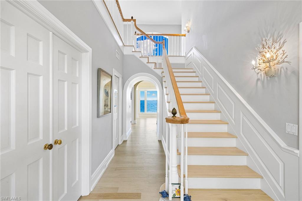 Stairs with arched walkways, wood finished floors, and a high ceiling