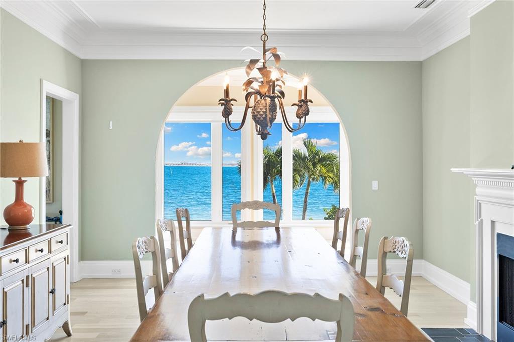 Dining area with light wood finished floors, crown molding, a chandelier, a water view, and a fireplace with flush hearth