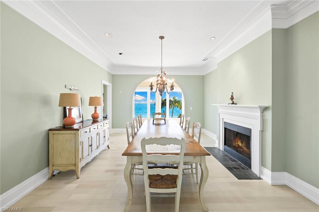 Dining space featuring light wood-type flooring, ornamental molding, a fireplace with flush hearth, a chandelier, and recessed lighting