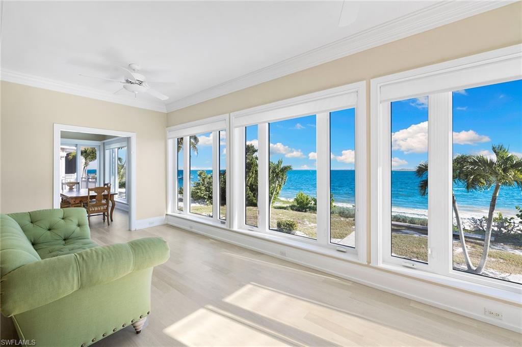 Sunroom / solarium with ornamental molding, view of water and beach, and wood finished floors