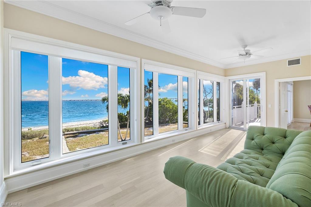 Sunroom featuring wood finished floors, ornamental molding, and view of water and beach