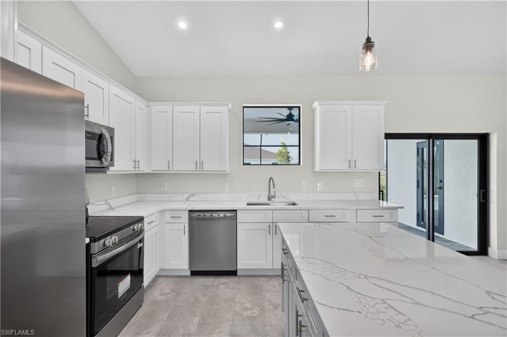 Modern kitchen featuring a central island with a waterfall countertop, white cabinetry, stainless steel appliances, and pendant lighting