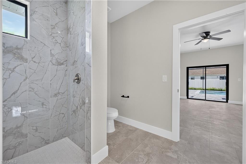 Spacious interior room featuring light grey walls, grey tile flooring, white baseboards, and a black ceiling fan with integrated lighting