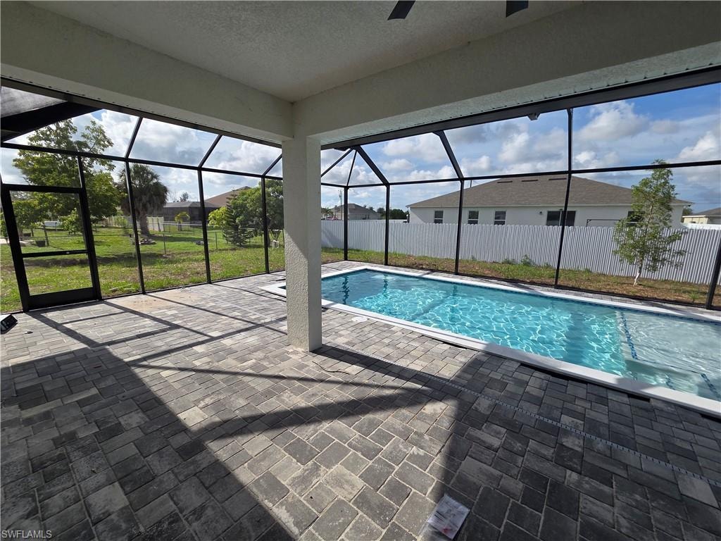 Expansive screened lanai featuring a rectangular swimming pool with a surrounding paver deck, a covered patio area with a ceiling fan, and a solid exterior door with a glass panel