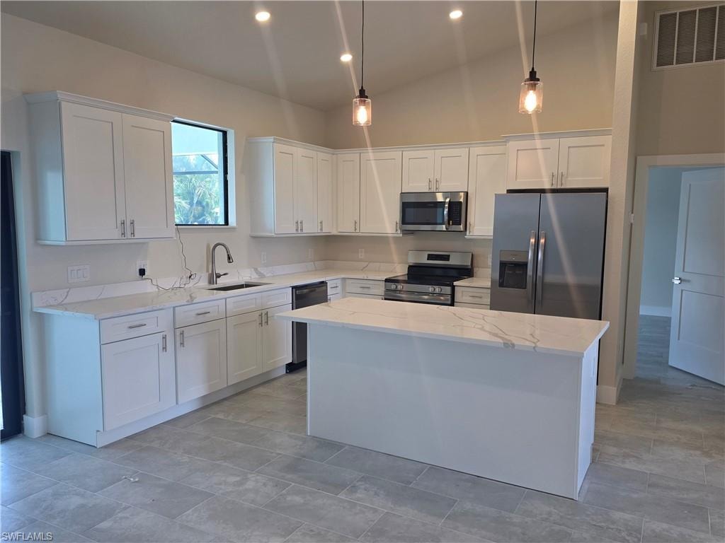 Kitchen featuring a center island, white cabinetry, stainless steel appliances, light-toned countertops, and pendant lighting