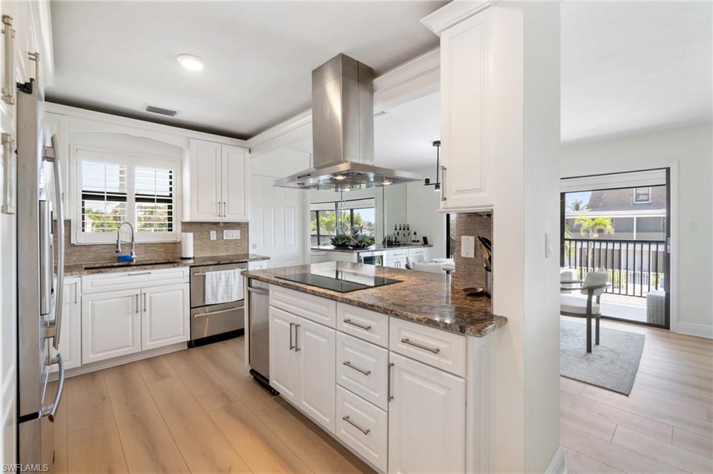 Kitchen with dark stone countertops, tasteful backsplash, light wood-style floors, white cabinetry, and island exhaust hood