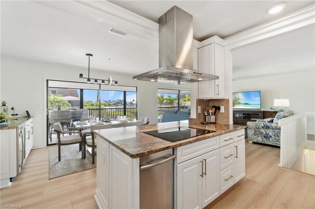 Kitchen with dark stone countertops, white cabinets, light wood-style floors, island exhaust hood, and backsplash