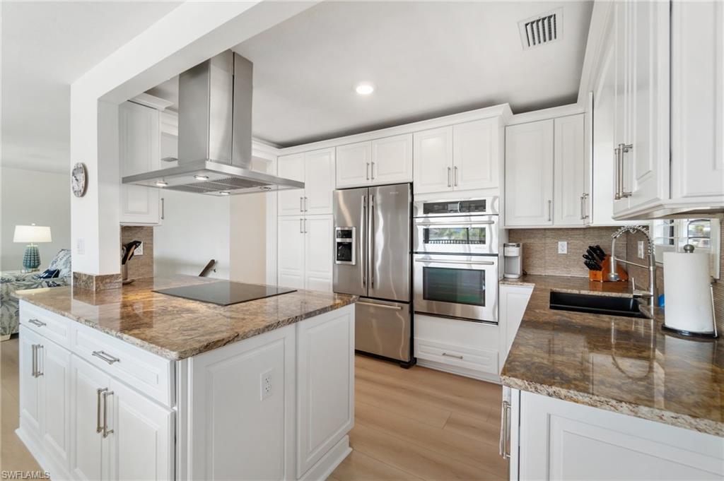 Kitchen with white cabinetry, island exhaust hood, dark stone countertops, decorative backsplash, and recessed lighting