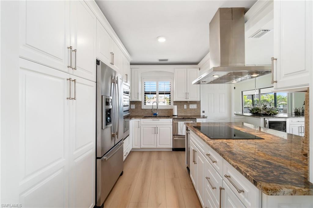 Kitchen with dark stone countertops, white cabinets, island range hood, stainless steel appliances, and recessed lighting