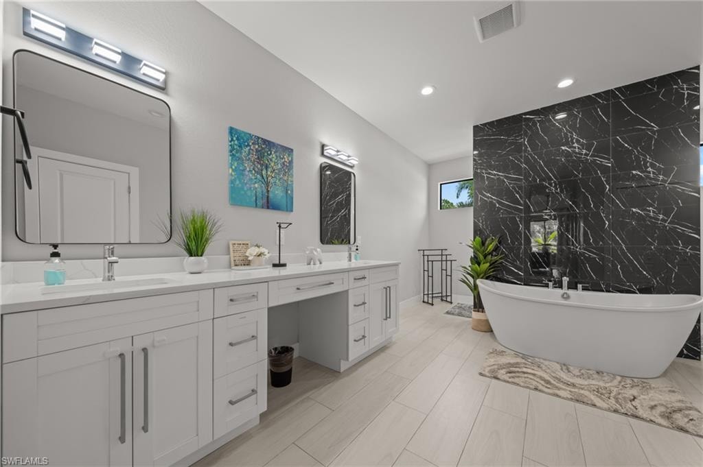 Full bathroom featuring double vanity, a freestanding bath, tile walls, and recessed lighting