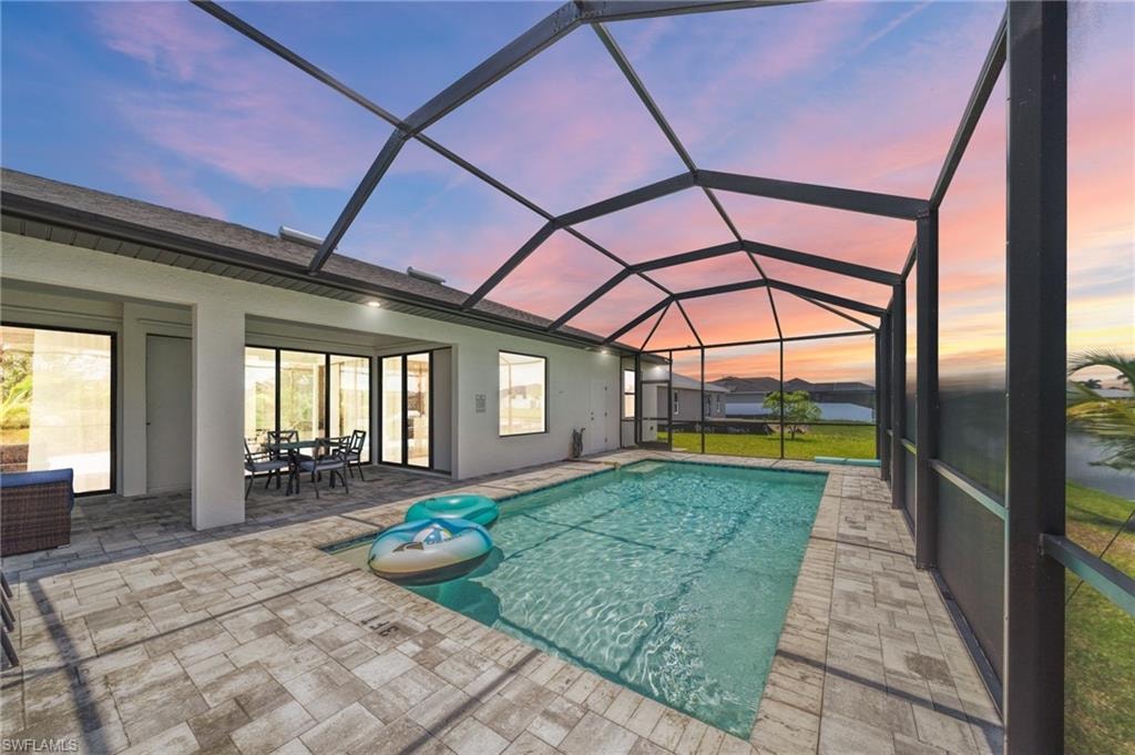 Pool at dusk with an outdoor pool, a patio area, a lanai, and outdoor dining area