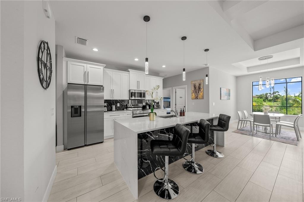 Kitchen featuring stainless steel appliances, white cabinetry, a kitchen island with sink, a kitchen breakfast bar, and light countertops
