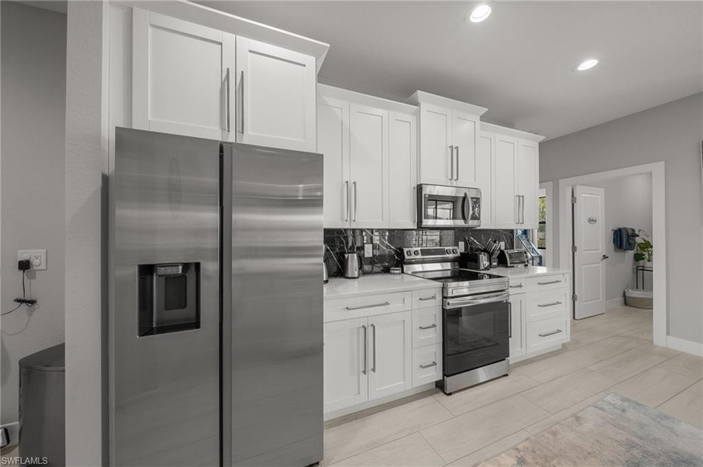 Kitchen featuring appliances with stainless steel finishes, tasteful backsplash, light countertops, recessed lighting, and white cabinetry
