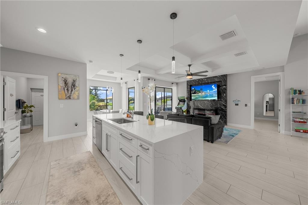 Kitchen featuring ceiling fan, white cabinetry, hanging light fixtures, a kitchen island with sink, and light stone countertops