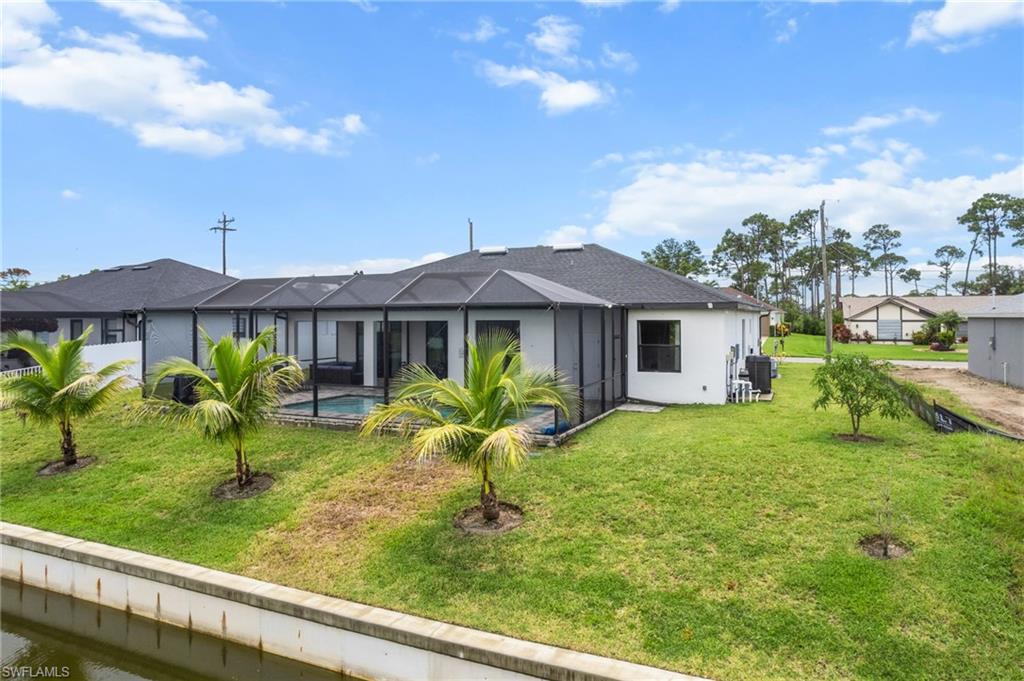 Rear view of property featuring stucco siding, a lanai, a lawn, and an outdoor pool