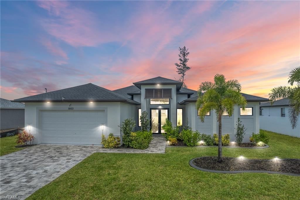 View of front of home with a garage, decorative driveway, a lawn, and a shingled roof