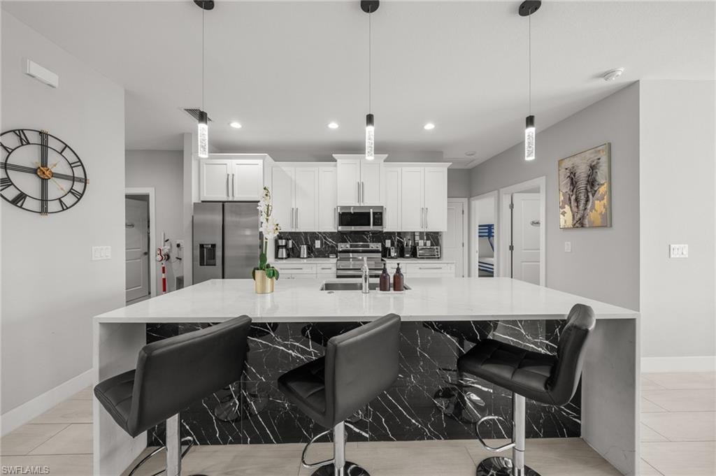 Kitchen featuring stainless steel appliances, decorative backsplash, a large island with sink, white cabinets, and recessed lighting