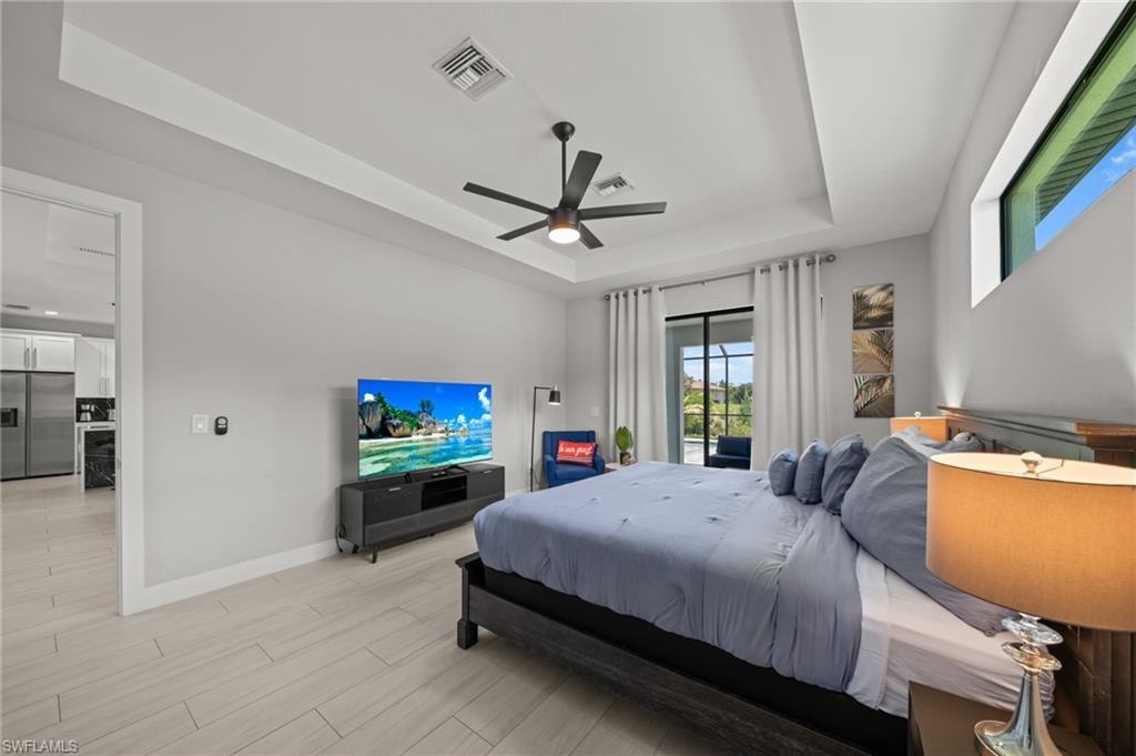 Bedroom featuring a raised ceiling, stainless steel fridge with ice dispenser, wood finish floors, and ceiling fan