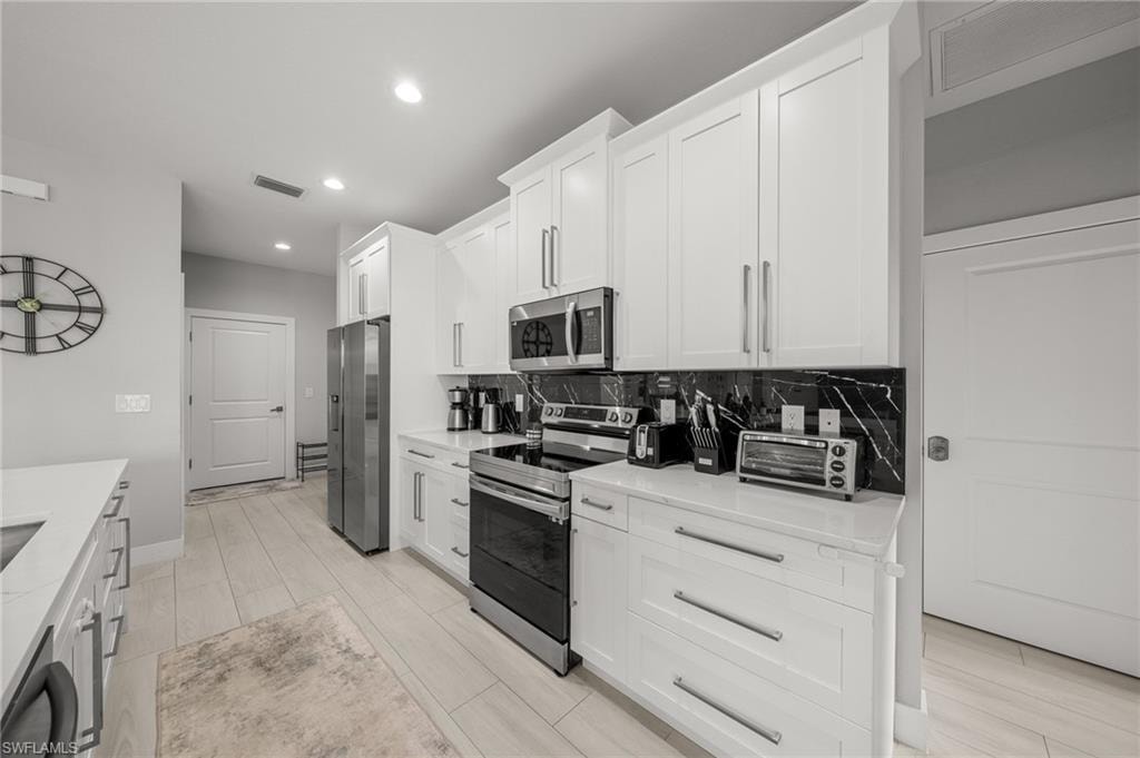 Kitchen with stainless steel appliances, light countertops, white cabinetry, recessed lighting, and backsplash