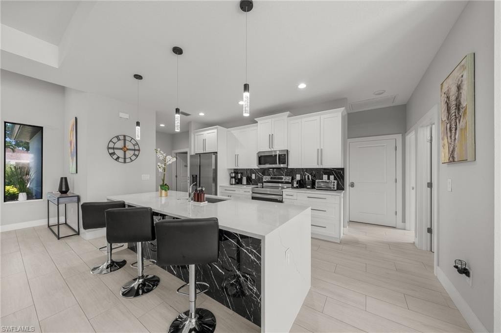 Kitchen with stainless steel appliances, a large island with sink, white cabinets, a breakfast bar, and decorative backsplash