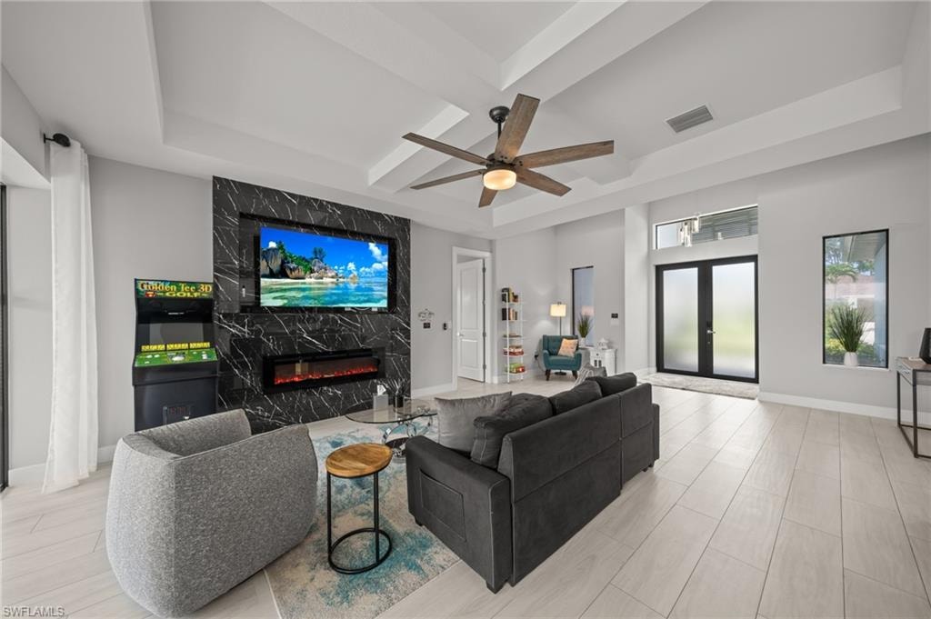Living room featuring a high end fireplace, a ceiling fan, french doors, coffered ceiling, and a raised ceiling