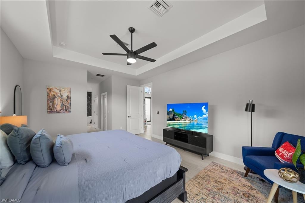 Bedroom with a raised ceiling, light wood finished floors, and a ceiling fan