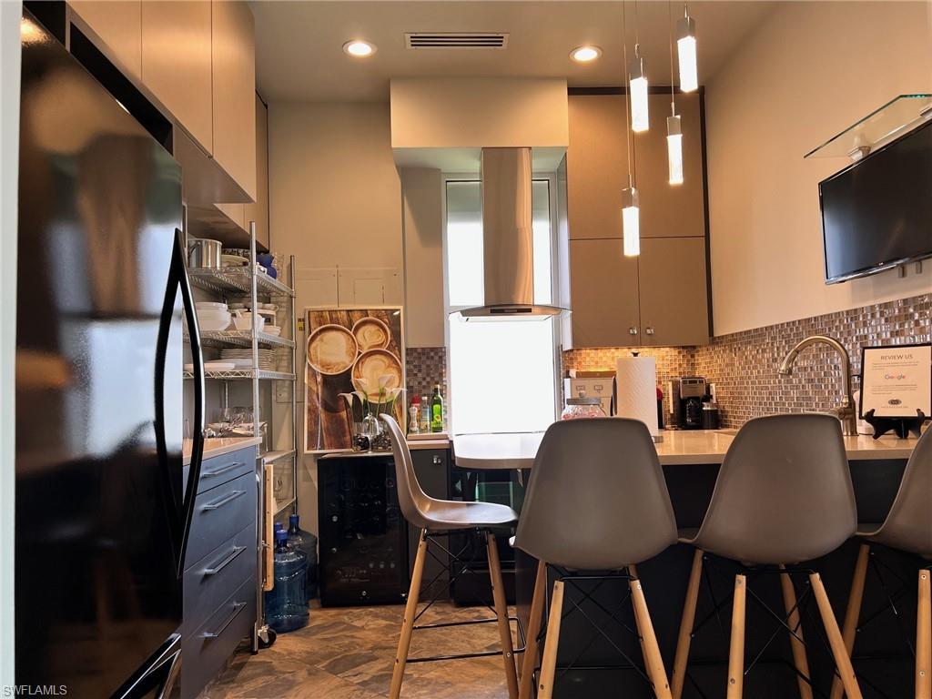 Kitchen featuring freestanding refrigerator, wall chimney range hood, a breakfast bar, decorative backsplash, and hanging light fixtures