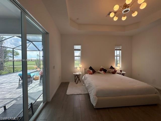 Bedroom featuring access to exterior, a tray ceiling, wood-type flooring, and a notable chandelier