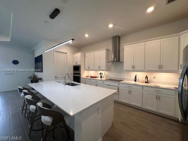Kitchen with wall chimney range hood, a kitchen island with sink, dark hardwood / wood-style floors, and white cabinets