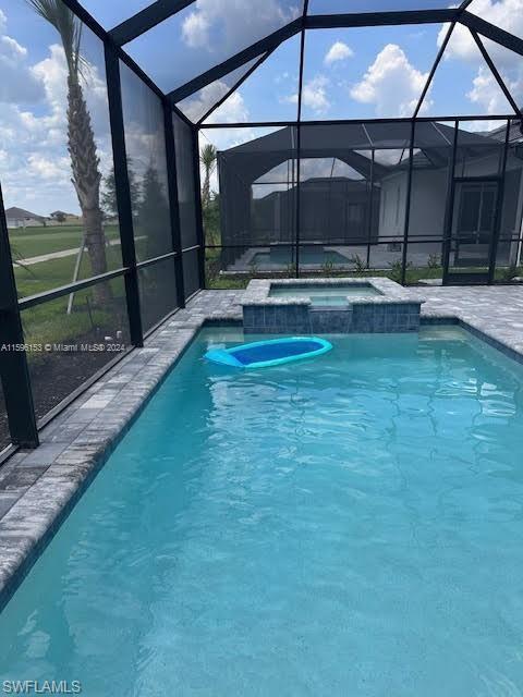 View of swimming pool with an in ground hot tub and glass enclosure