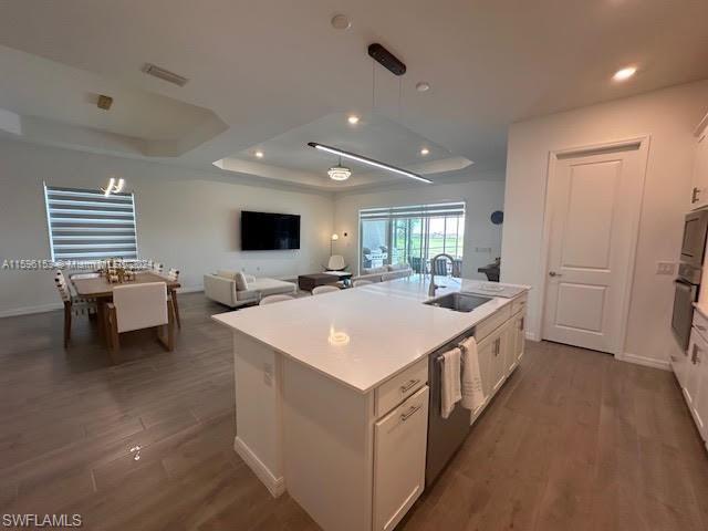 Kitchen with dishwasher, pendant lighting, a raised ceiling, and hardwood / wood-style floors