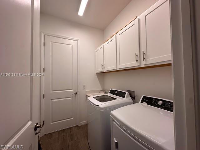 Washroom featuring dark wood-type flooring, washing machine and clothes dryer, and cabinets